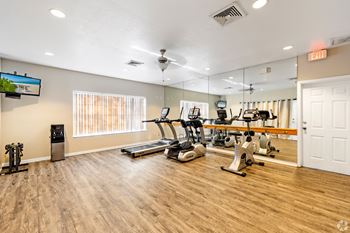 A gym with treadmills, elliptical machines, and a television.